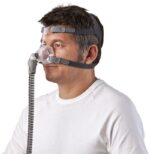 Man wearing a CPAP nasal mask with headgear and a hose, shown from the side.