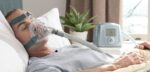 Man lying in bed wearing a CPAP mask, with a CPAP machine on the bedside table next to him.