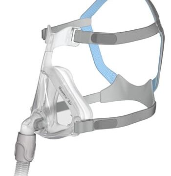 Clear CPAP face mask with gray and blue straps and a hose connector, shown from a side angle.