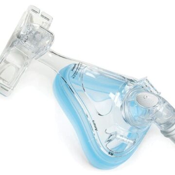 Clear full-face CPAP mask with blue silicone lining and plastic headgear attachment, viewed from above.