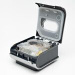 A CPAP machine humidifier chamber with its lid open, showing the water reservoir inside.