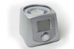 A gray medical device with a digital screen and a round button on the front.