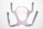 A pink and gray CPAP mask headgear with four straps laid flat on a white background.