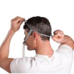 Man wearing a CPAP mask, adjusting the head strap, viewed from behind.