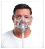Man wearing a CPAP mask with a hose, used for sleep apnea therapy, against a plain background.