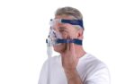 Man wearing a CPAP mask with straps, adjusting the fit on his face, against a white background.