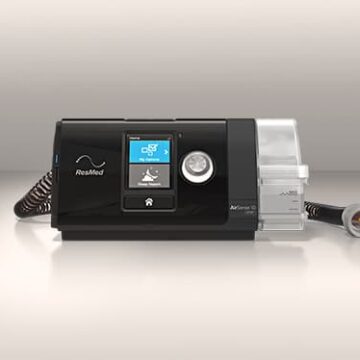 Black ResMed CPAP machine with display screen, hose, and attached clear water chamber on a neutral background.