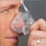 Close-up of a person holding a clear oxygen mask to their face, with a gray background.