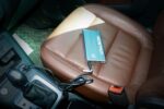 A portable power bank with a cable lies on a brown leather car seat next to the gear shift.