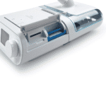 A white CPAP machine with an open slot showing a blue filter and a clear water chamber on the side.