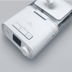 White medical device with a display screen, buttons, and a clear water chamber, shown on a gray background.