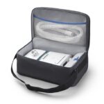 A CPAP machine with hose neatly packed in a black travel carrying case with an open lid.
