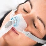 Person lying down with eyes closed, wearing a nasal CPAP mask for breathing assistance.
