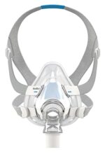 Full-face CPAP mask with clear plastic frame, gray headgear straps, and white mask clips, viewed from the front.