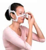 Woman wearing a CPAP nasal mask, adjusting the mask with her hand against a white background.