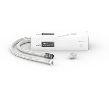 CPAP tubing and connector with a ResMed AirMini setup pack box in the background on a white surface.