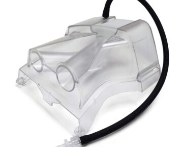 Clear plastic respiratory mask with two ports and a black hose attached on a white background.