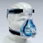 A mannequin wearing a clear and blue CPAP face mask with head straps.