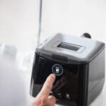 A person presses a button on a black kitchen appliance with a digital display.