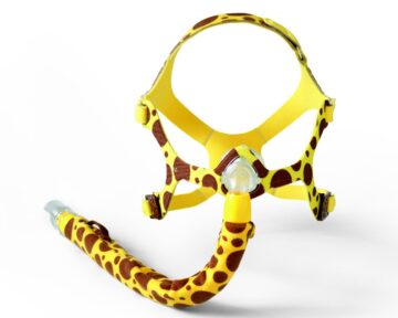 A CPAP mask with a yellow and brown giraffe print design on a white background.