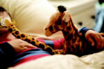 A child in striped pajamas holds a giraffe toy while lying in bed.