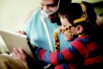 A man and a child wearing CPAP masks look at a tablet together.