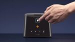A hand pressing a button on a modern black kitchen appliance with a digital display.