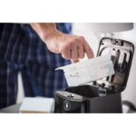 A person removes a water tank from a CPAP machine, wearing blue plaid pajamas.