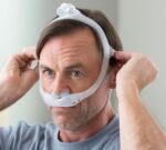 Middle-aged man adjusting a CPAP nasal mask on his face for sleep apnea therapy.