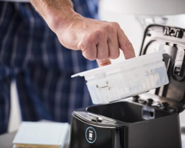 A person places a plastic container into a black CPAP machine for cleaning or maintenance.