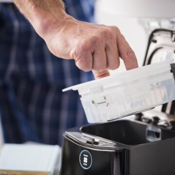 A person places a plastic container into a black CPAP machine for cleaning or maintenance.