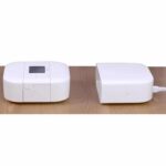 Two white electronic devices on a wooden surface, one with a display screen and buttons, the other with a power light.