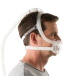 Man wearing a CPAP mask with headgear and hose, viewed from the side against a plain background.