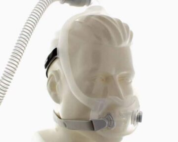 A mannequin head wearing a full-face CPAP mask with attached tubing for sleep apnea therapy.