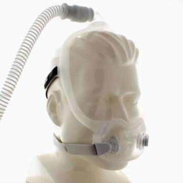 A mannequin head wearing a full-face CPAP mask with attached tubing for sleep apnea therapy.