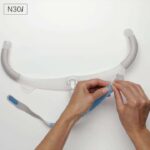 A person is putting on a ResMed AirFit N30i Nasal CPAP Mask on a white wall.