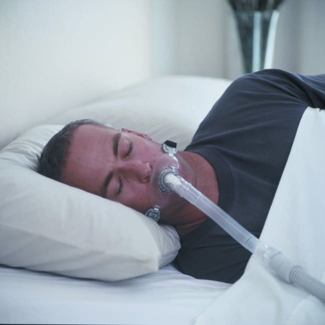 A man sleeping in bed with a Fisher & Paykel Oracle 452 Oral CPAP Mask (Fit Pack).