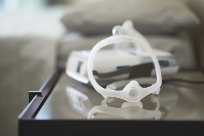 A nebulizer and a Respironics DreamWisp Nasal CPAP Mask (Fit Pack) sitting on a table next to a bed.