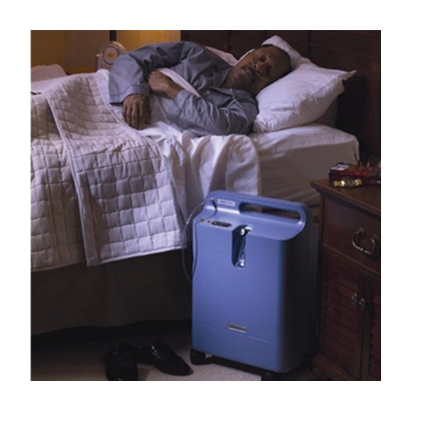 A man resting in bed next to a Respironics Everflo Stationary Concentrator.