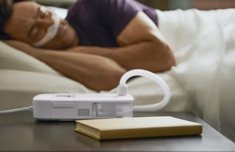A man is using a Phillips Respironics Dreamstation Go Heated Humidifier in bed.