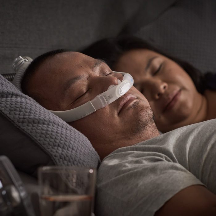 A man and woman sleeping in bed with a ResMed AirFit P30i Nasal Pillow CPAP Mask.