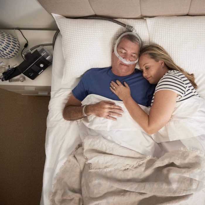 A man and woman sleeping in bed with a ResMed AirFit P30i Nasal Pillow CPAP Mask.