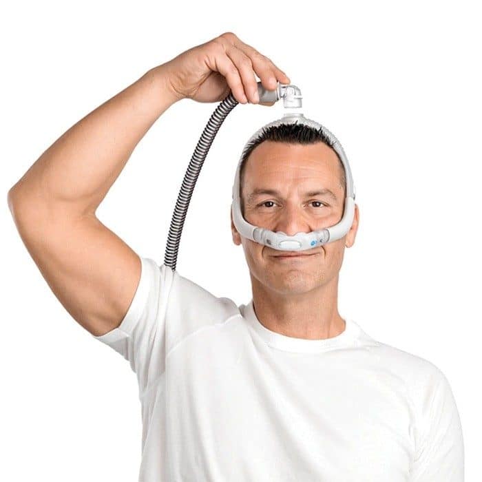 A man wearing a ResMed AirFit P30i Nasal Pillow CPAP Mask with headgear has a hose attached to his head.