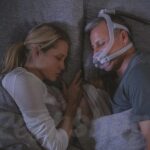 A man and woman using the ResMed AirFit F30i Full Face CPAP Mask while sleeping in bed.