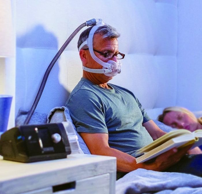 A man reading a book while wearing a ResMed AirFit F30i Full Face CPAP Mask.