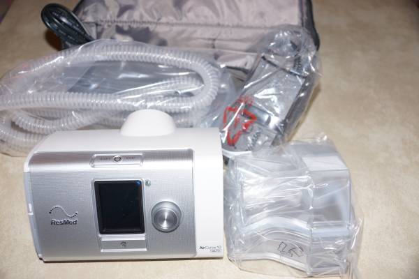 A discounted ResMed AirCurve S10 VAuto Bi-Level Machine Package with HumidAir Humidifier & Mask is next to a bag on a table.