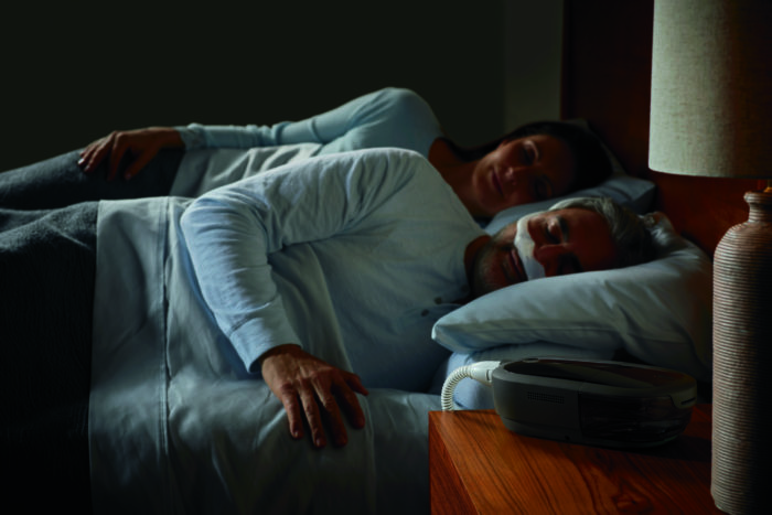 A man and a woman sleeping peacefully with their Respironics Dreamstation 2 Auto CPAP Advanced with Humidifier, Cell Modem & Standard Tubing.