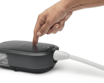 A hand is pointing to a new device connected to a cord: Brand New Respironics Dreamstation 2 Auto CPAP Advanced with Humidifier, Cell Modem & Standard Tubing.