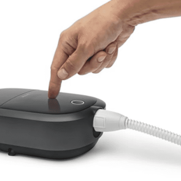 A hand is pointing to a new device connected to a cord: Brand New Respironics Dreamstation 2 Auto CPAP Advanced with Humidifier, Cell Modem & Standard Tubing.