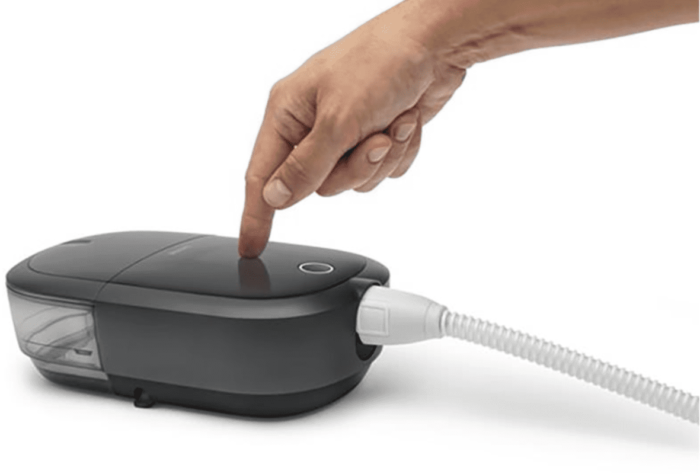 A hand is pointing to a new device connected to a cord: Brand New Respironics Dreamstation 2 Auto CPAP Advanced with Humidifier, Cell Modem & Standard Tubing.